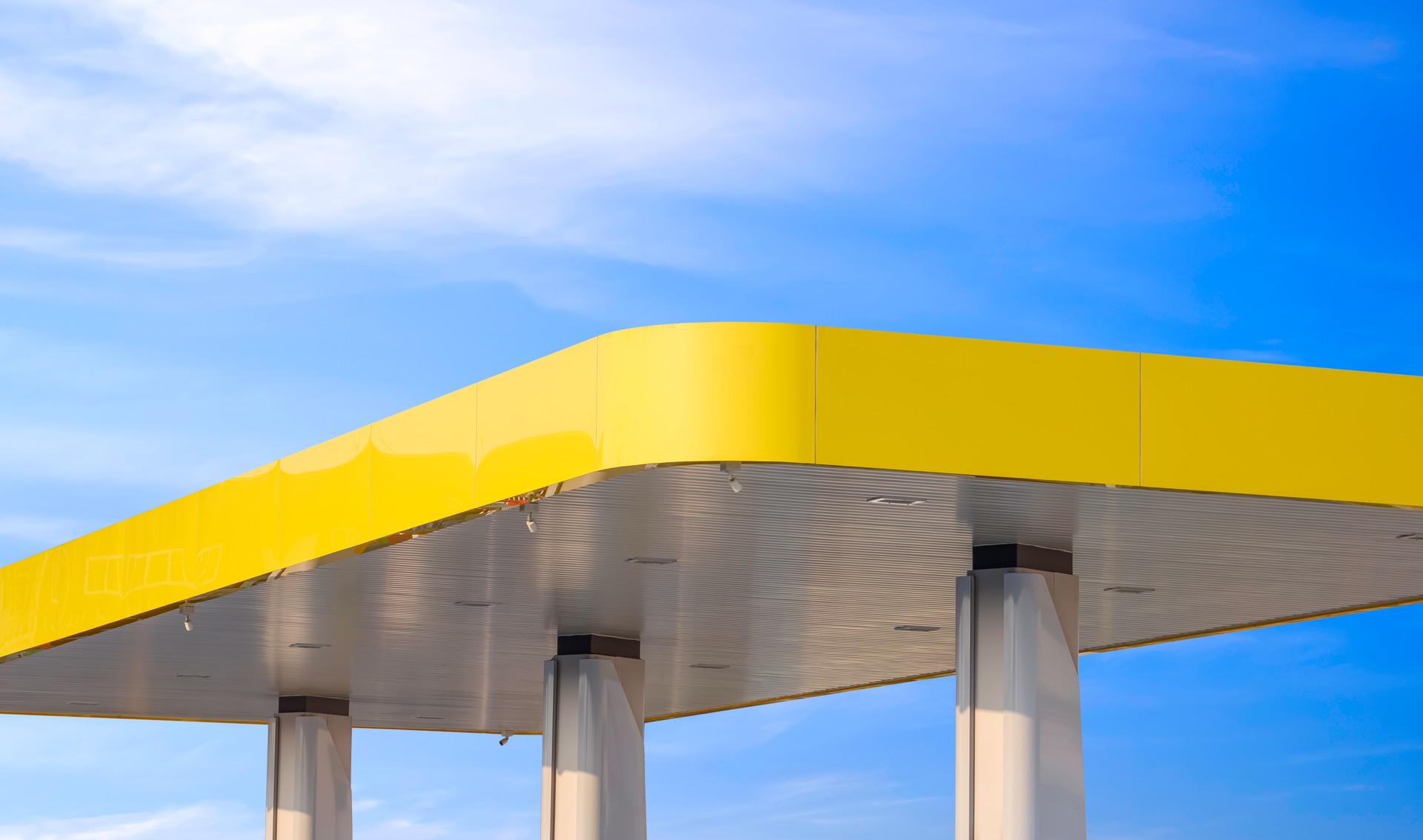 Modern yellow canopy roof of outdoor distribution service point with columns of gas station against blue sky background